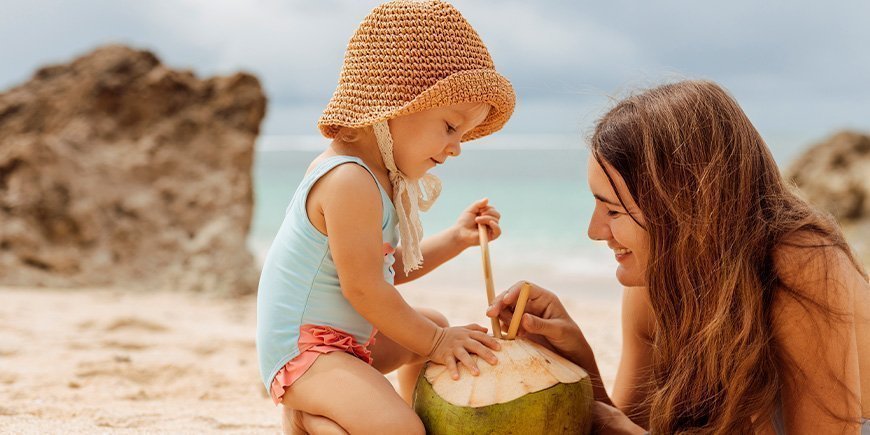 Mamma och dotter dricker från en kokosnöt på en strand i Thailand